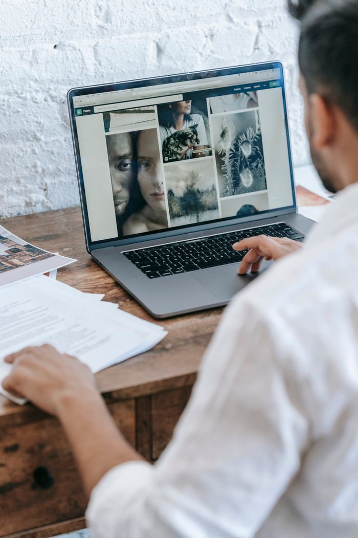 Vue de dos d’un freelance masculin anonyme, assis à une table et travaillant sur un projet sur ordinateur portable dans une pièce lumineuse en journée